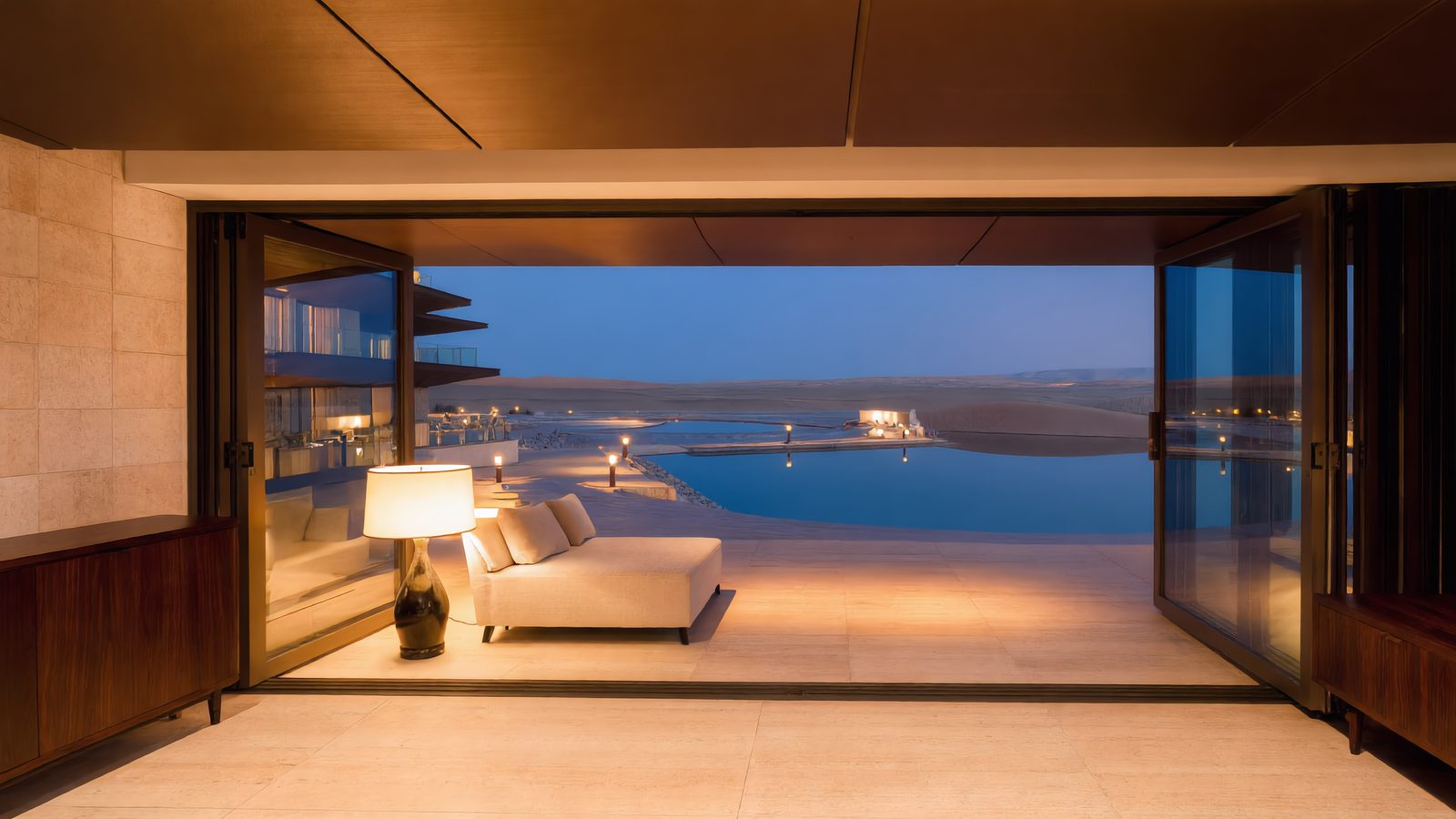 A living room on the third terrace at dusk, the glazing open to the lagoon